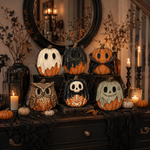 A Halloween-themed decorative display featuring multiple carved pumpkins styled as ghosts, owls, skeletons, and crouching pumpkins, arranged on a dark wooden console table with black lace, candles, lanterns, and dried branches in a warmly lit interior setting.
