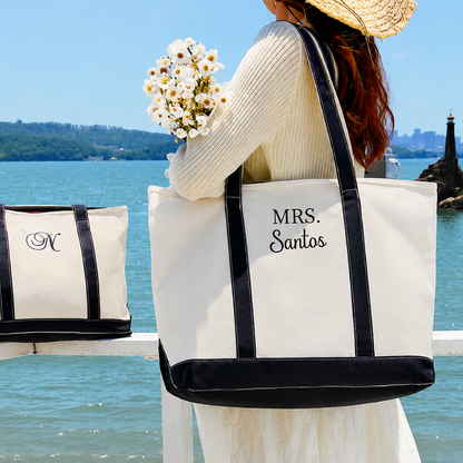 Woman holding a personalized tote bag by a waterfront with mountains and a lighthouse in the background.