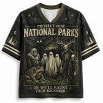 A black short-sleeve V-neck t-shirt with a detailed graphic print on the front. The graphic features a spooky national parks theme with a toad, ghosts, a skeleton, a bat, and a deer skull, accompanied by the text 'PROTECT OUR NATIONAL PARKS OR WE'LL HAUNT YOUR BACKYARD'.