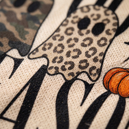Close-up of a Halloween-themed graphic print on a textured beige fabric, featuring a ghost with a leopard print pattern, black and white zebra stripes, and an orange pumpkin.