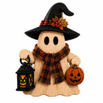 A wooden Halloween ghost decoration holding a black lantern and a carved pumpkin, wearing a black witch hat with a plaid band and orange leaf accent, and a plaid scarf.