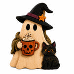 A Halloween-themed wooden figurine of a ghost wearing a black witch hat with an orange star and holding an orange pumpkin mug with hot cocoa, accompanied by a black cat on a white background.